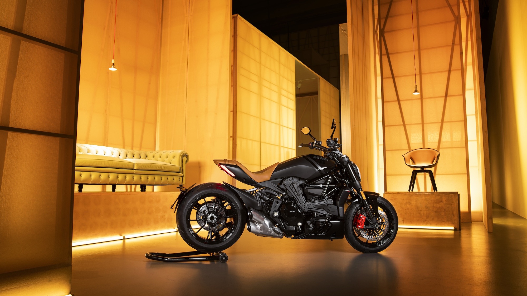 Ducati XDiavel motorcycle displayed in an amber-lit lounge setting alongside a Poltrona Frau armchair