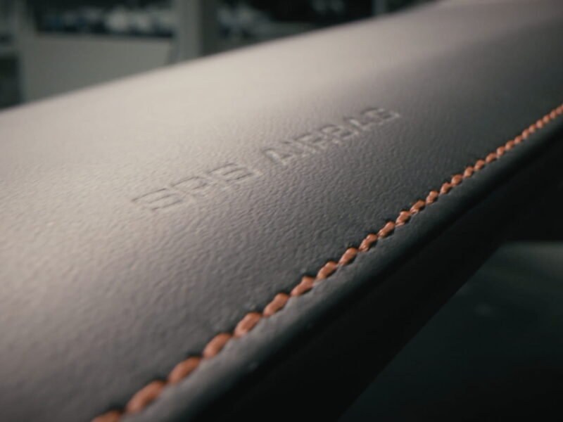 Close-up of a leather dashboard panel with orange stitching and a laser-scored line for airbag deployment