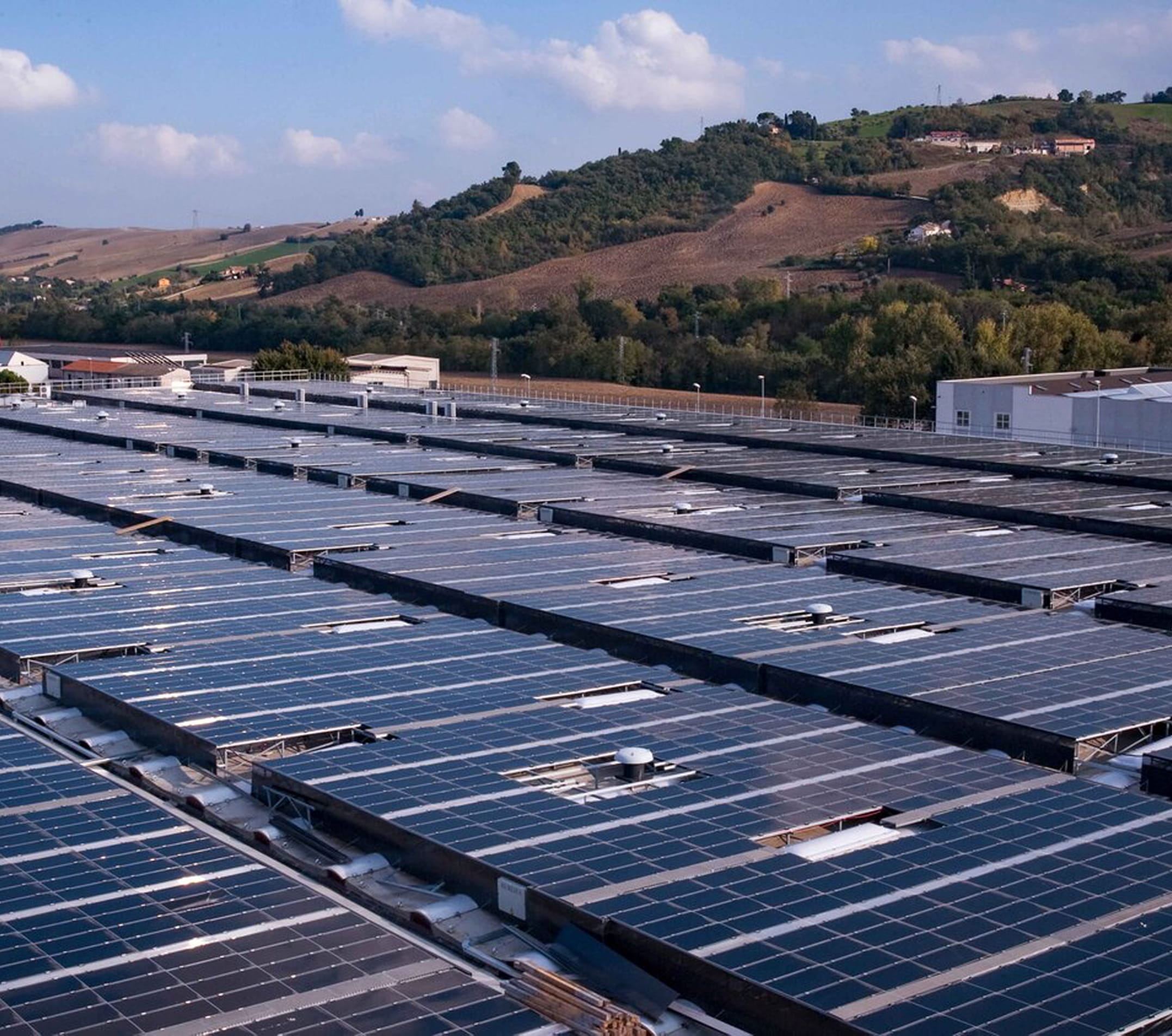 Environment-square Aerial view of solar panels installed on a factory roof surrounded by green hills